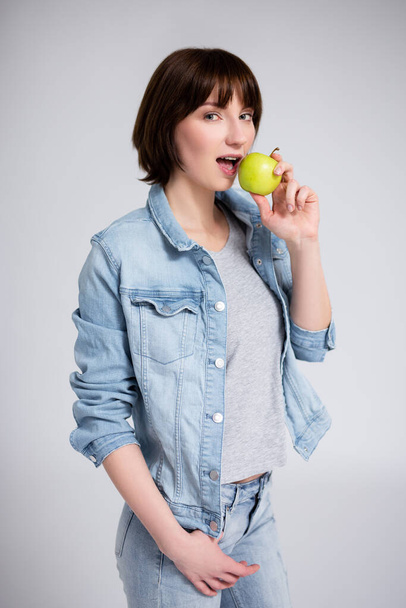 dentistry and orthodontics concept - portrait of young woman or teenage girl with braces on teeth biting green apple over gray background - Photo, Image