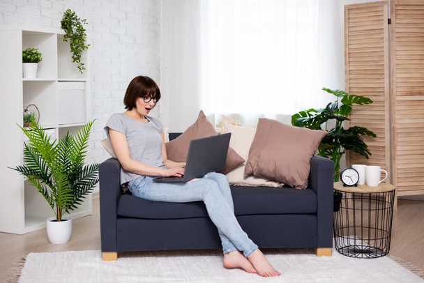 online shopping and sale concept - portrait of surprised young woman using laptop in bright living room - Фото, зображення