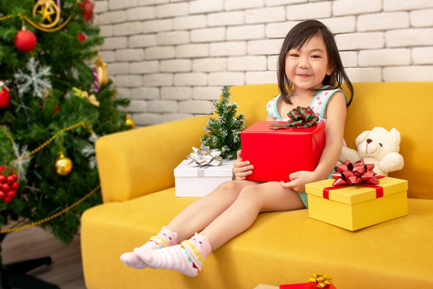 Vánoční a prázdninový koncept. Šťastná holka s dárkovou krabicí. Dívka v vánoční čepici ruce dárek zabalený se zlatým papírem a červenou stuhou. Veselé Vánoce a šťastný nový rok. - Fotografie, Obrázek