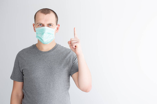 Coronavirus-Schutz und Quarantäne-Konzept - Mann in medizinischer Maske zeigt Idee oder Warnschild vor weißem Hintergrund - Foto, Bild
