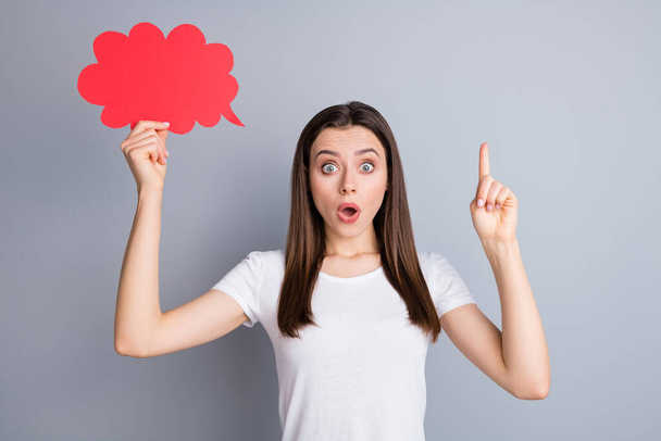 Portrait of astonished girl hold red paper card speech bubble get incredible idea raise index finger up impressed wear good look clothes isolated over gray color background - 写真・画像