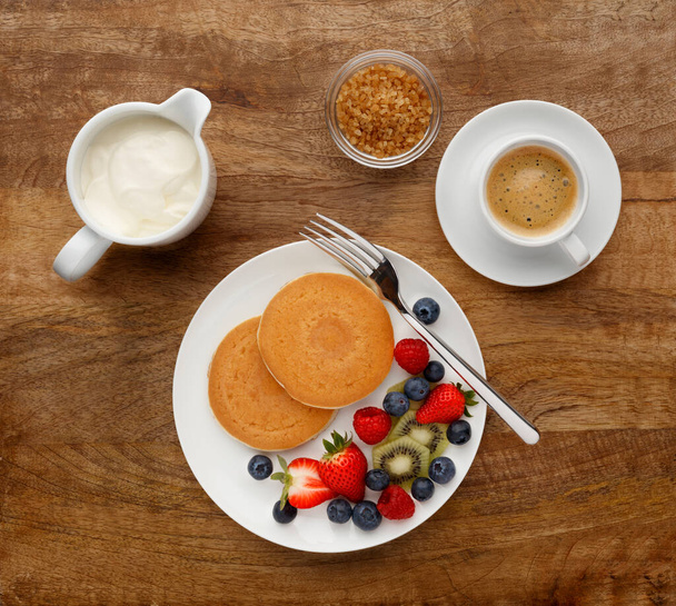 Continental breakfast of a Pancakes, fruit, and coffee, shot on a antique wood table top, from above. - Foto, imagen