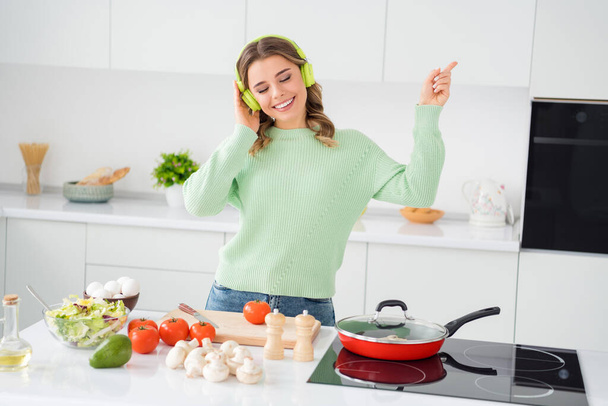 Portrait of her she nice attractive lovely dreamy cheerful wavy-haired girl cooking homemade lunch listening music having fun spending day in modern light white kitchen indoors - Photo, Image