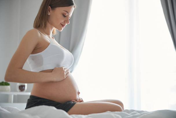Woman smiling and looking pleased to feel child inside the belly - Photo, image