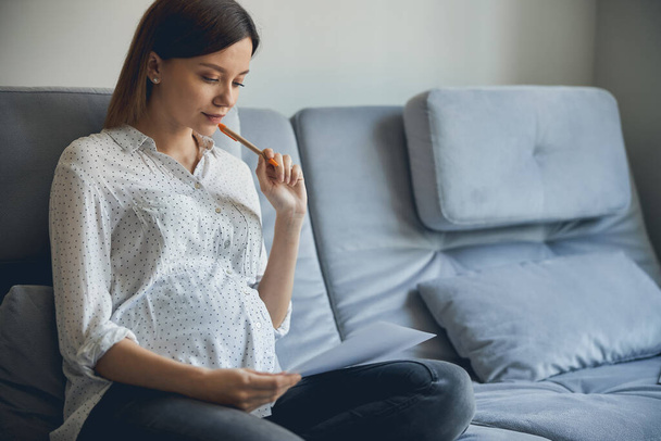 Nachdenkliche Schwangere plant ihren Monat und schaut auf Kalender - Foto, Bild