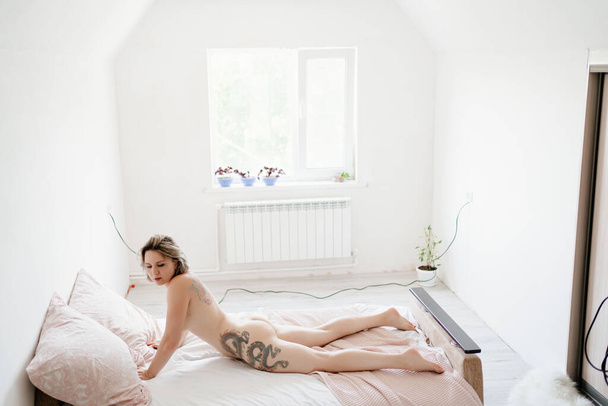 rear view. sexy girl with tattoo. Nude woman lying on bed in small bedroom. - Foto, Bild