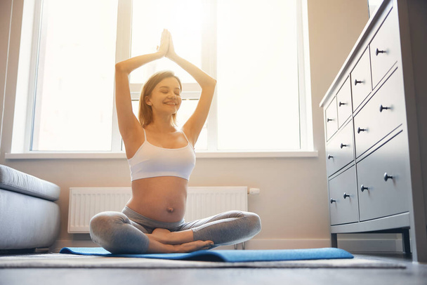 Возбужденная дама наслаждается йогой дома во время беременности
 - Фото, изображение