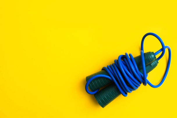 Blue fitness skipping rope for jumping with plastic handles on yellow background - Φωτογραφία, εικόνα