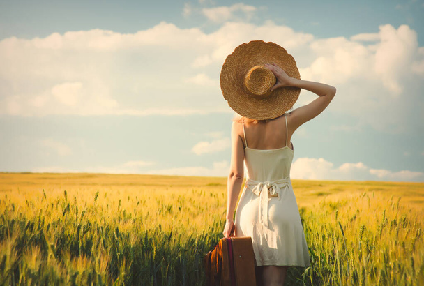 Блок жінка в капелюсі з валізою в пшеничному полі під час заходу сонця
  - Фото, зображення