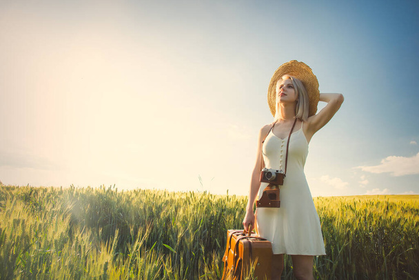 Ξανθιά γυναίκα με βαλίτσα και κάμερα στο χωράφι με το σιτάρι το καλοκαίρι - Φωτογραφία, εικόνα