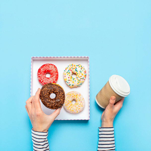 Female hands are holding a donut and a cup of coffee on a blue background. Concept confectionery store, pastries, coffee shop. Banner. Flat lay, top view. - Фото, зображення