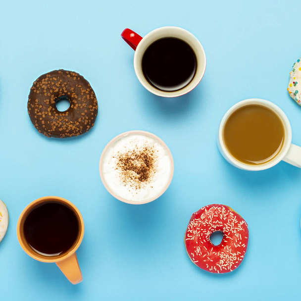 Tasty donuts and cups with hot drinks, coffee, cappuccino, tea on a blue background. Concept of sweets, bakery, pastries, coffee shop, meeting, friends, friendly team. Square. Flat lay, top view. - Photo, Image