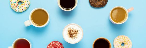 Lekkere donuts en kopjes met warme dranken, koffie, cappuccino, thee op een blauwe achtergrond. Concept van snoep, bakkerij, gebak, coffeeshop, vergadering, vrienden, vriendelijk team. Een spandoek. Vlakke lay, bovenaanzicht. - Foto, afbeelding