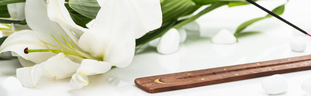 palo de aroma en soporte de madera cerca de lirio sobre fondo blanco, tiro panorámico
 - Foto, Imagen