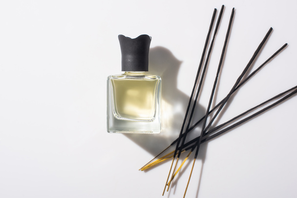 top view of aroma sticks near perfume in bottle on white background - Fotoğraf, Görsel