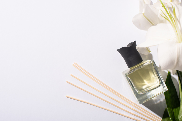 Draufsicht auf Duftstäbchen mit Parfüm in der Flasche in der Nähe von Lilien auf weißem Hintergrund - Foto, Bild