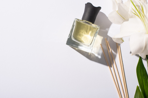 vista superior de palos de aroma con perfume en botella cerca de lirios sobre fondo blanco
 - Foto, Imagen