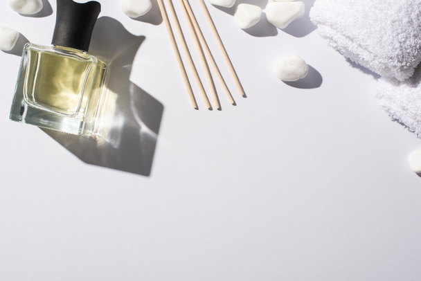 bovenaanzicht van aroma sticks met parfum in fles in de buurt van spa stenen en handdoek op witte achtergrond - Foto, afbeelding