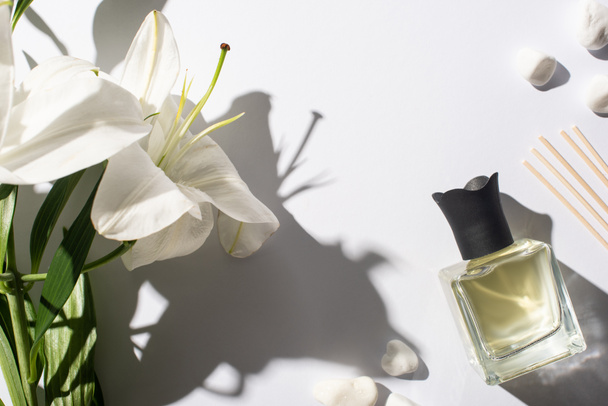 górny widok paluszki aromatyczne z perfum w butelce w pobliżu kamieni i kwiat lilii na białym tle - Zdjęcie, obraz