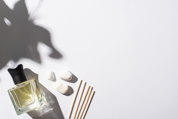 bovenaanzicht van aroma sticks met parfum in fles in de buurt van stenen op witte achtergrond - Foto, afbeelding