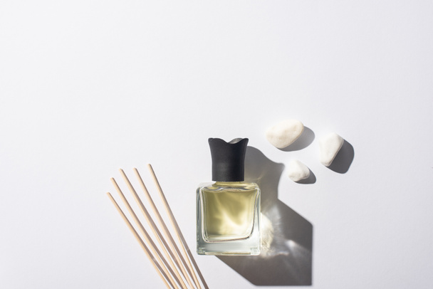 vue de dessus des bâtons d'arôme avec parfum en bouteille près de pierres sur fond blanc - Photo, image