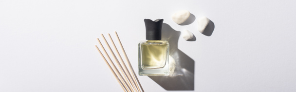 vista superior de palos de aroma con perfume en botella cerca de piedras sobre fondo blanco, plano panorámico
 - Foto, imagen
