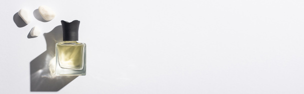 vrchní pohled na domácí parfém v láhvi u kamenů na bílém pozadí, panoramatický záběr - Fotografie, Obrázek