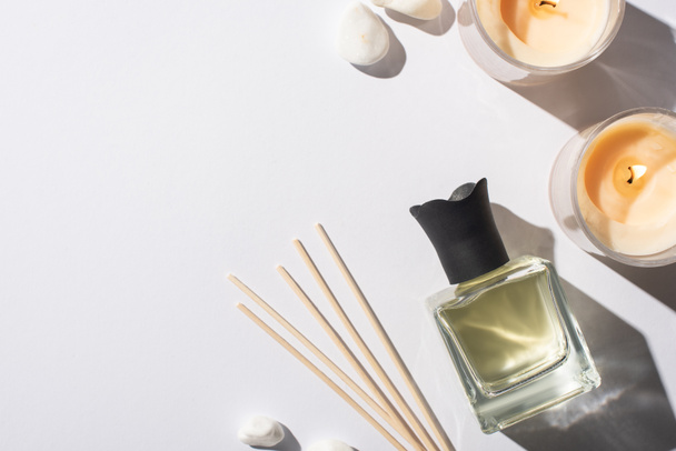 bovenaanzicht van aroma sticks met parfum in fles in de buurt van stenen en kaarsen op witte achtergrond - Foto, afbeelding