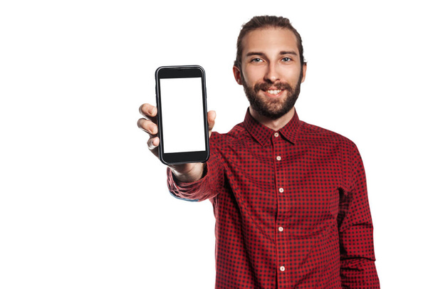 A young smiling man shows a smartphone screen on a white background. Isolate Place for advertising and advertising labels. - Fotografie, Obrázek