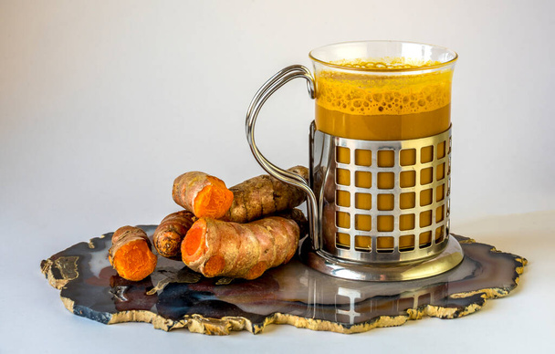 Chá tumérico fresco na xícara com raiz fresca na placa, fundo branco
 - Foto, Imagem