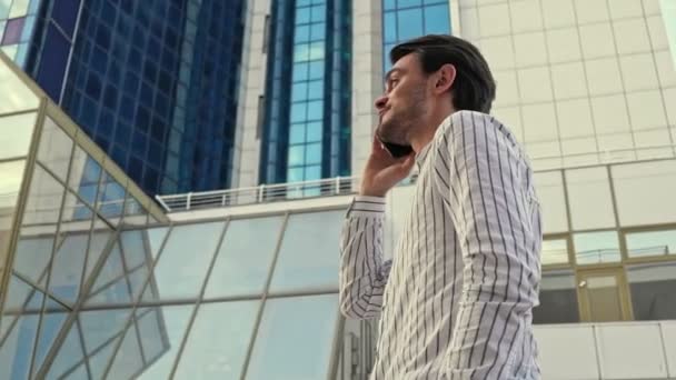 Een bottom view van een succesvolle knappe jonge zakenman met een bril op praat op zijn smartphone terwijl hij op een pier loopt - Video