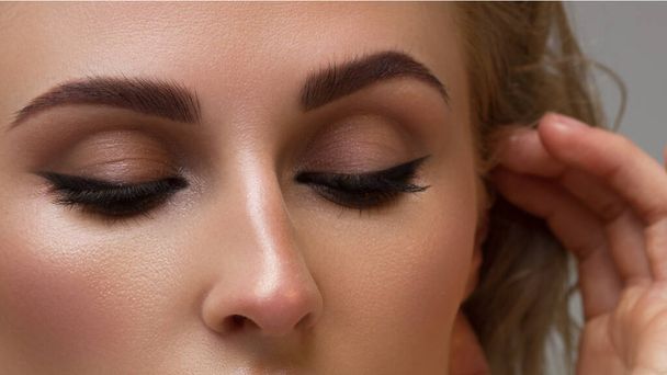 Elegance close-up female eye with dark brown eyeshadow. Macro shot of part of the face of a beautiful woman. Wellness, cosmetics and makeup. smooth beautiful eyebrows and eyelashes - 写真・画像