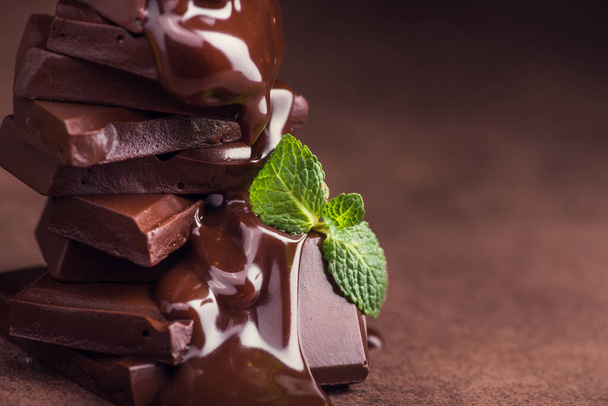 melted chocolate pouring into a piece of chocolate bars with green mint leaf on a table - Foto, immagini