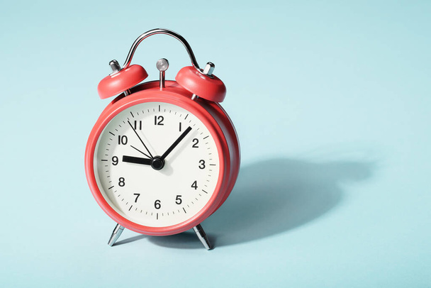 Reloj despertador rojo con sombra sobre fondo azul. Siete minutos después de las nueve en el reloj - Foto, imagen