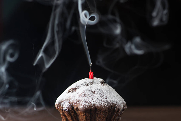Pudralı çikolatalı pasta ve dumanlı kırmızı mum. Doğum gününün sonunda, siyah arka planda. - Fotoğraf, Görsel