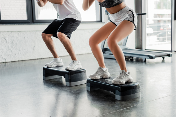 cropped view of sportsman and sportswoman exercising on step platforms  - Foto, Imagen