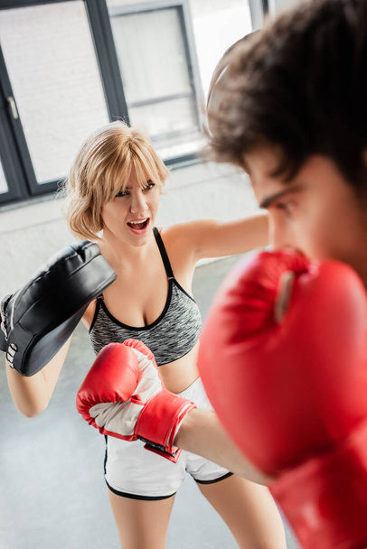 вибірковий фокус емоційної дівчини в боксерських майданчиках вправи зі спортсменом в тренажерному залі
  - Фото, зображення