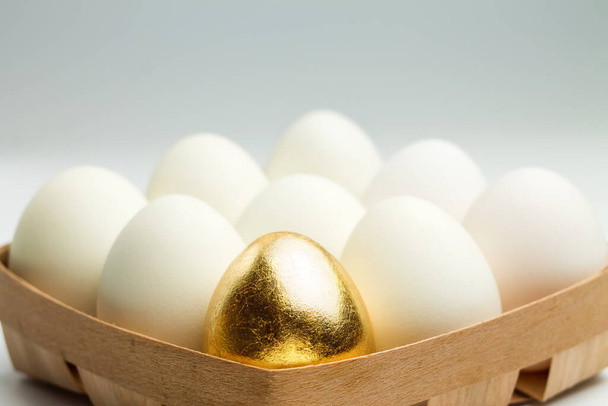 Ein goldenes Ei zwischen weißen Eiern in einer Holzkiste. Einzigartigkeitskonzept. - Foto, Bild
