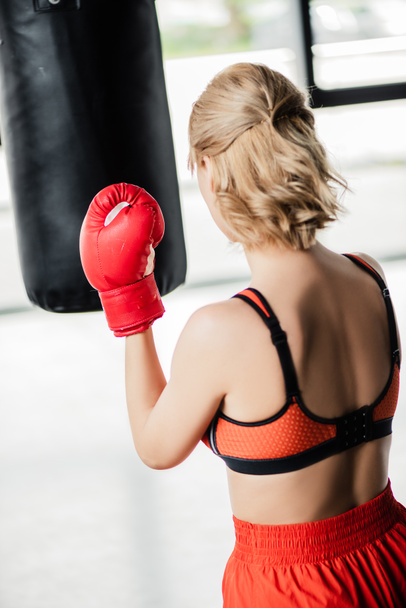 vista posteriore della ragazza sportiva in guanti da boxe che si esercita con il sacco da boxe  - Foto, immagini