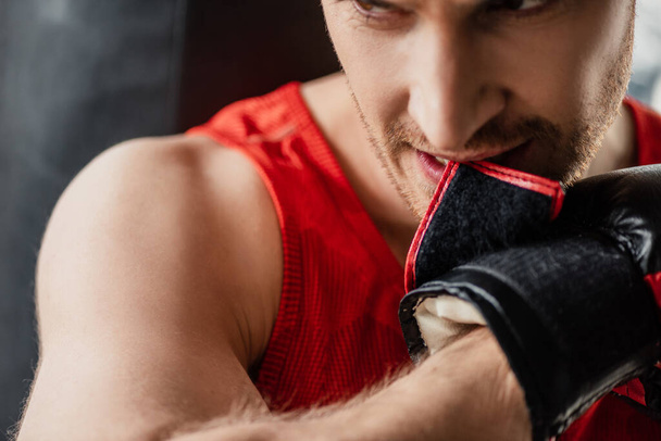 zbliżenie sportowca w odzieży sportowej gryzienie rękawica bokserska w siłowni  - Zdjęcie, obraz