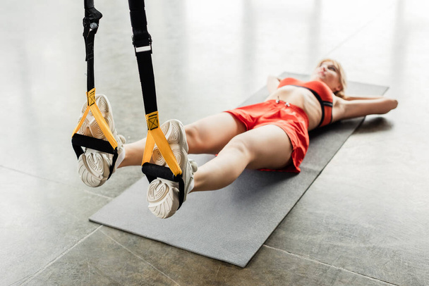 selective focus of athletic young woman in sportswear exercising with resistance bands while lying on fitness mat  - Fotó, kép