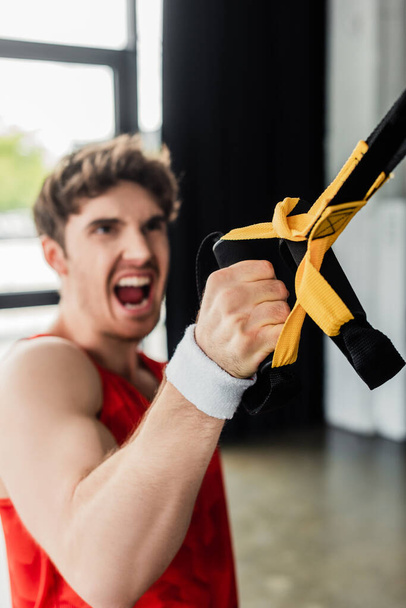 selective focus of sportive man screaming while working out with elastics in gym  - Foto, Imagen