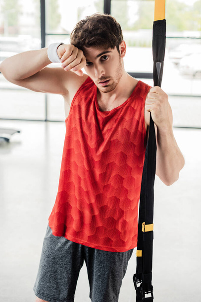 exhausted sportsman standing and touching resistance bands in gym  - Photo, Image