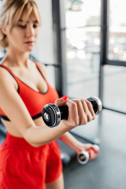 selective focus of sportive woman working out with dumbbells in sports center  - Foto, imagen