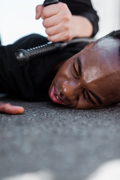 enfoque selectivo del hombre afroamericano detenido acostado en el suelo cerca de la policía con porra, concepto de racismo
  - Foto, Imagen