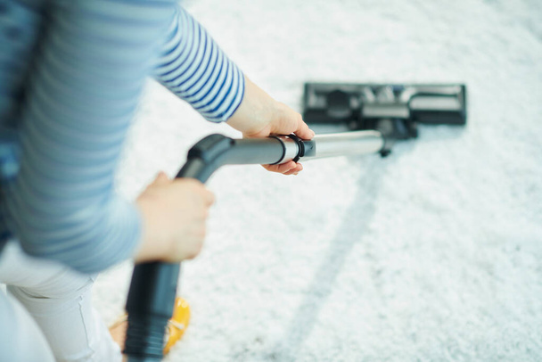 Closeup on woman in the living room in sunny day vacuuming white fluffy carpet. - Foto, afbeelding
