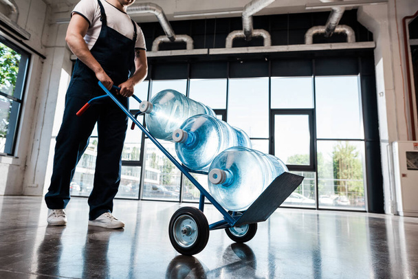 oříznutý pohled na doručovatele držícího ruční vozík s lahvemi čištěné vody  - Fotografie, Obrázek