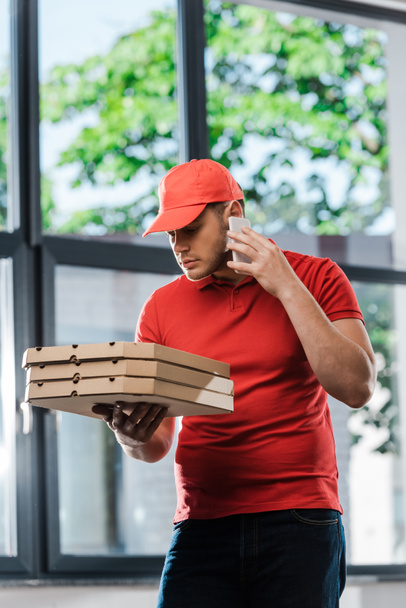 delivery man in cap μιλώντας στο smartphone και κρατώντας κουτιά πίτσα  - Φωτογραφία, εικόνα