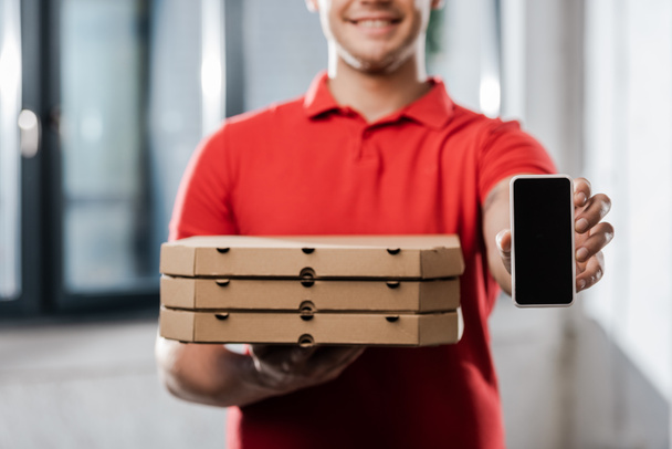 cropped view of happy delivery man in cap holding smartphone with blank screen and pizza boxes  - Fotoğraf, Görsel