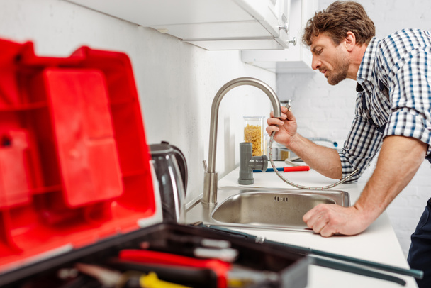 Foco selectivo del fontanero que sostiene la tubería metálica cerca del grifo de la cocina y la caja de herramientas
  - Foto, Imagen